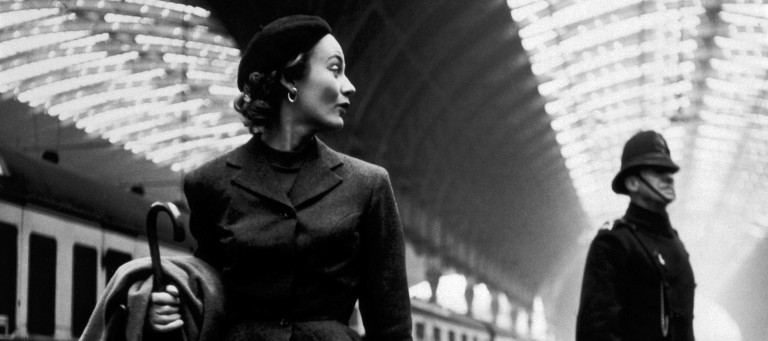 Photograph of a woman and a policeman at a train station by Toni Frissell, published by Harper's Bazaar in 1951